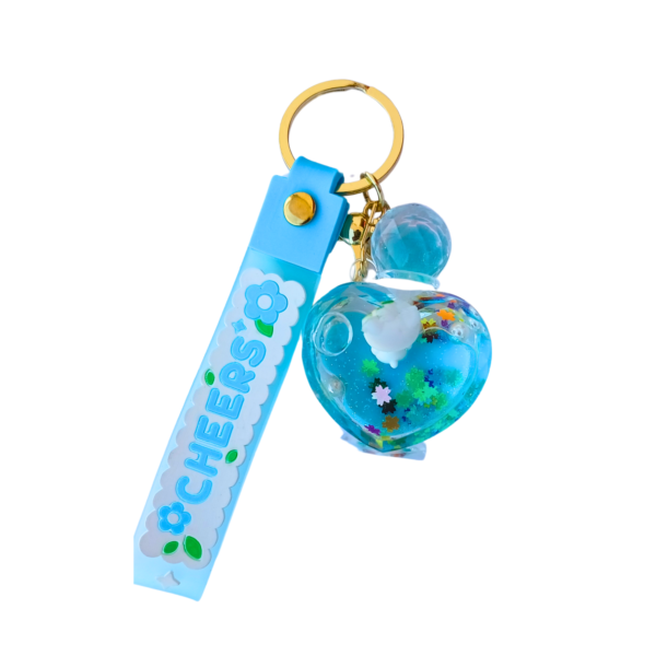 A blue floating heart liquid keychain with floral confetti and a tiny bear inside, attached to a gold keyring with a blue "CHEERS" silicone strap.