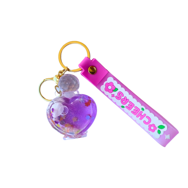 A purple floating heart liquid keychain with floral confetti and a tiny bear inside, attached to a gold keyring with a pink "CHEERS" silicone strap.