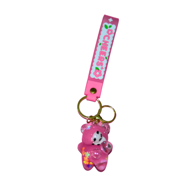 A pink glitter-infused resin bear keychain with a panda face, attached to a gold keyring and a pink "CHEERS" silicone strap.