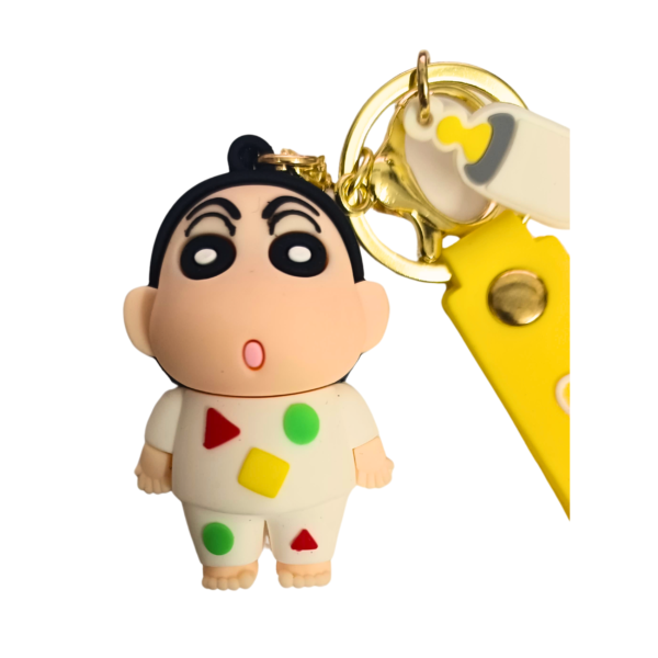 A Shinchan keychain featuring him in a white geometric-patterned outfit, attached to a yellow "Good Luck" silicone strap and a gold keyring.